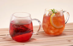Two glass mugs with red and orange beverages on wooden surface with lemon slices