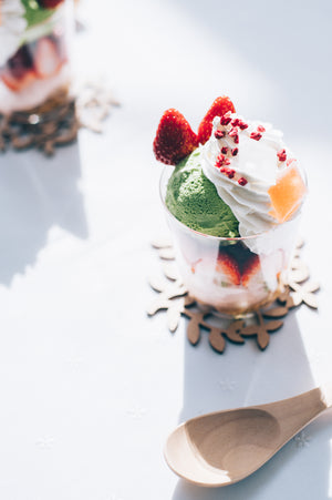 Close-up of layered glass dessert with pistachio ice cream, cream topping, strawberry, and garnish.