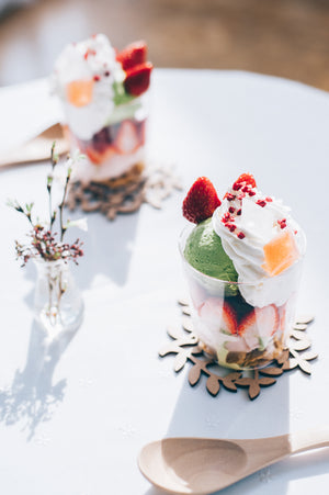 Decorated glass dessert with pistachio ice cream and strawberry beside fresh flowers in vase.