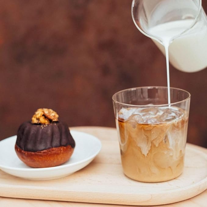 Milk pours into an iced coffee drink next to a chocolate pastry with walnut topping on a wooden board.