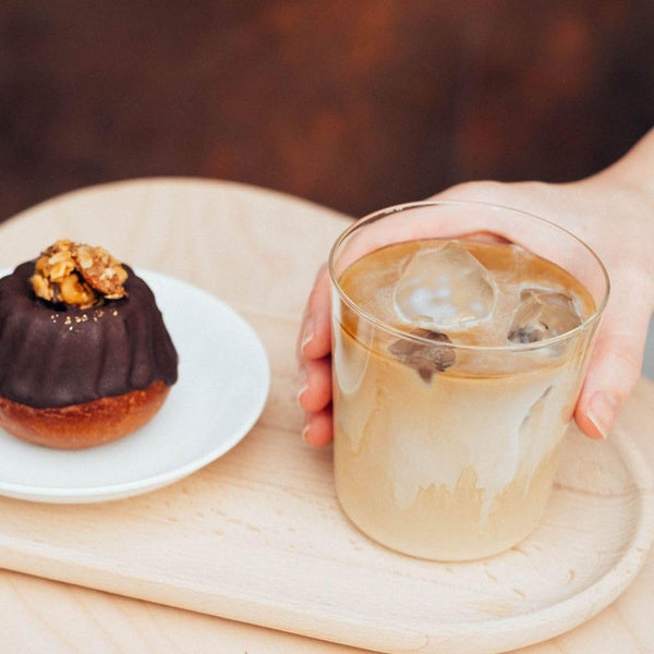 Person holding a glass filled with iced coffee and milk, displayed beside a chocolate pastry.