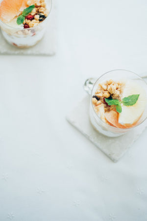 Two glasses filled with layered dessert, granola, dried fruit, and mint leaf garnish.