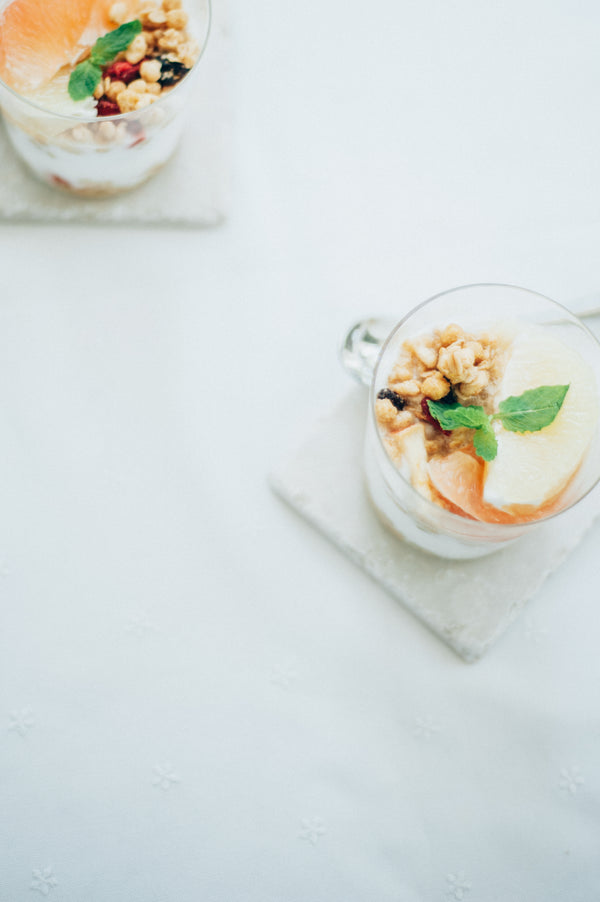 Two glasses filled with layered dessert, granola, dried fruit, and mint leaf garnish.