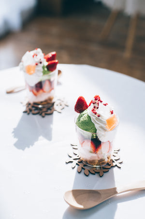Elegant glass dessert topped with pistachio ice cream, whipped cream, fresh strawberry, and red crumble.