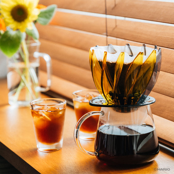 Assembled yellow and black Suiren dripper on carafe with coffee poured and two glasses nearby.