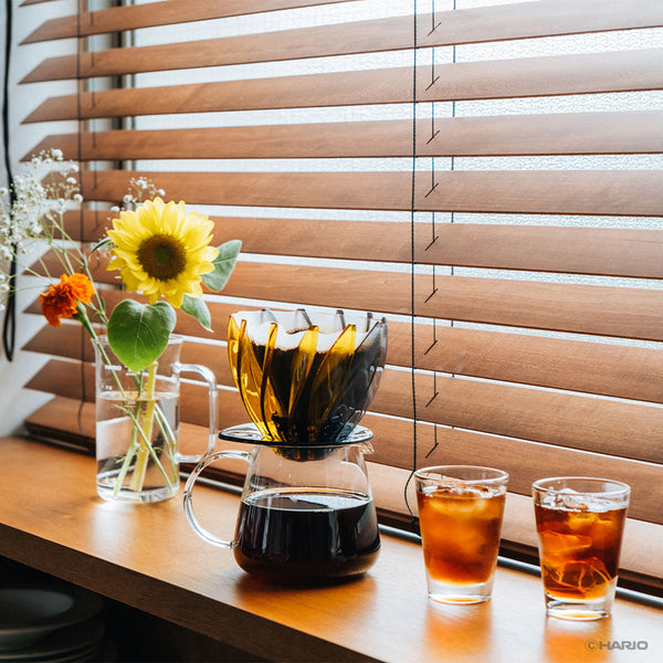 Suiren dripper with yellow petals on wooden table beside fresh flowers and beverage glasses.
