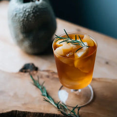Hario 300mL glass goblet filled with amber iced beverage and ice, garnished with fresh rosemary sprig.