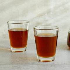 Two clear glass shot glasses filled with amber-colored liquid on a marble surface.