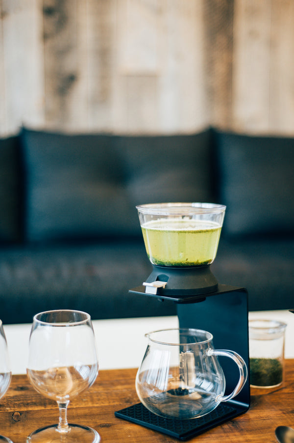 Overhead view of pale green tea in Largo dripper positioned above empty server in minimalist setting.