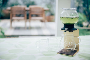 Tall Largo dripper with dark steeped tea displayed on white surface with outdoor backdrop.