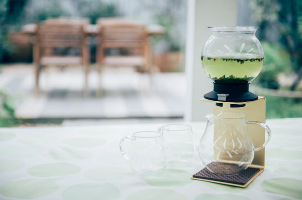 Tall Largo dripper with dark steeped tea displayed on white surface with outdoor backdrop.