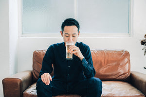 Man drinking from double-walled glass, eyes closed, wearing dark blue shirt