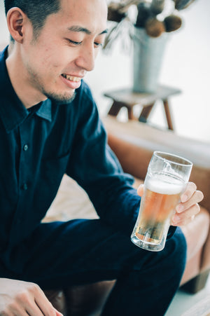 Man holding tall beer glass with white foam head, wearing navy button-up shirt