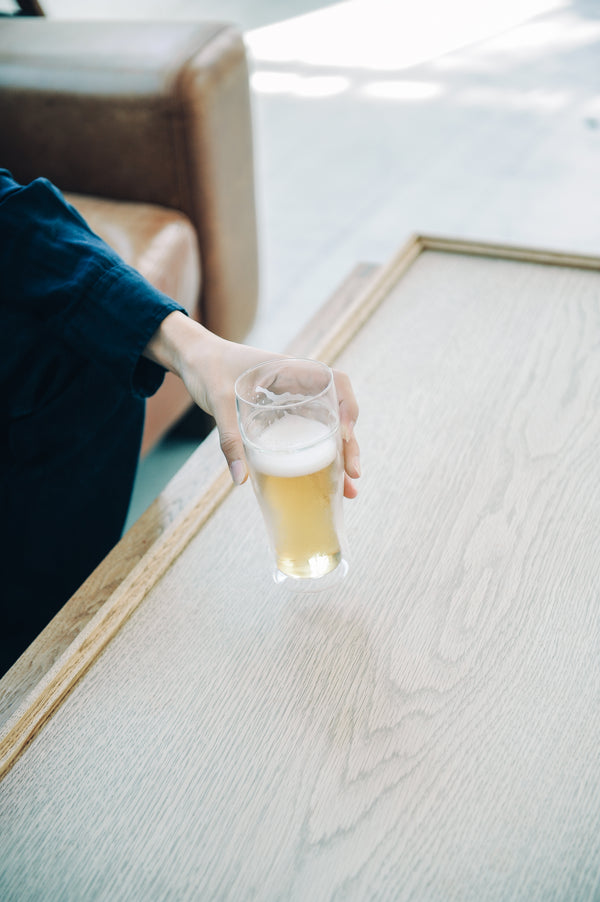 Hand holding double-walled beer glass with layered golden and white beverage on wooden table