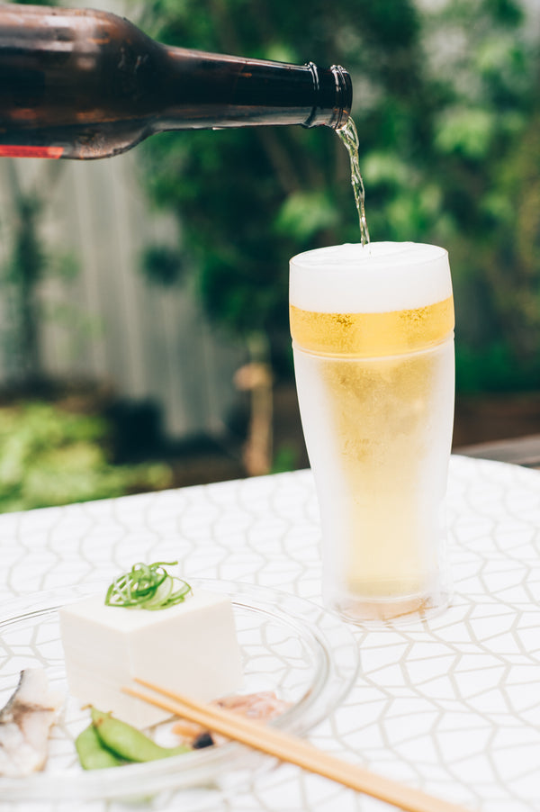 Close-up of beer bottle neck pouring into glass with visible foam and layering effect