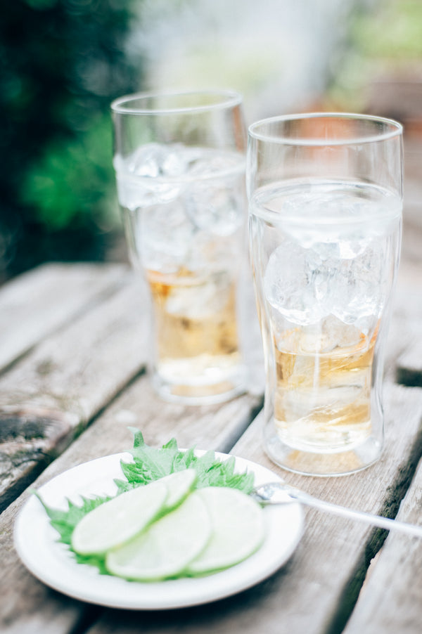 Two tall glasses with iced tea or cola and ice cubes on gray wooden surface with garnish