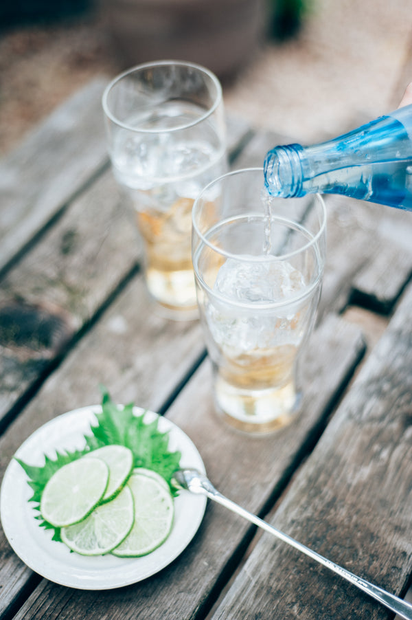 Blue water bottle pouring into double-walled glass beside iced beverage on weathered deck
