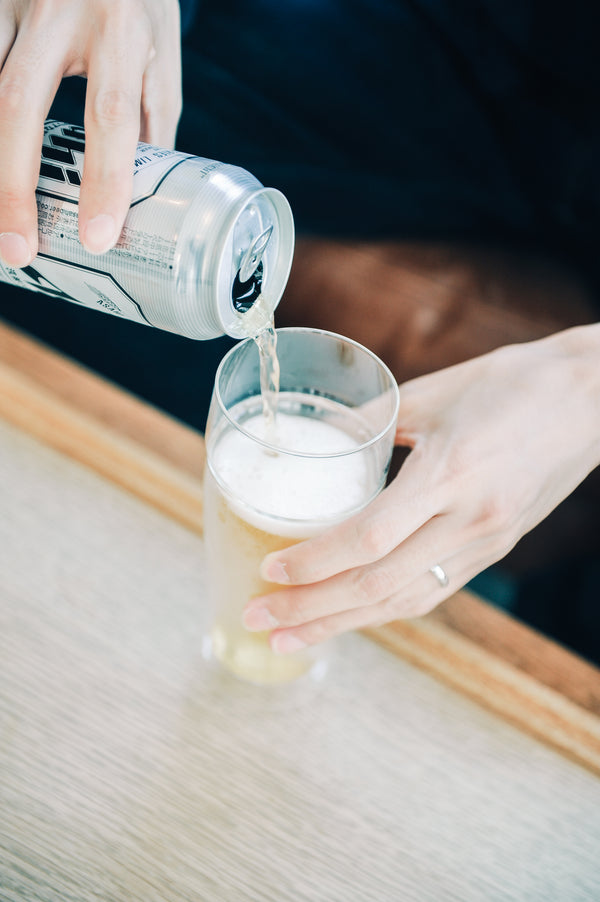 Hands pouring white foam from pitcher into layered beer glass containing golden liquid