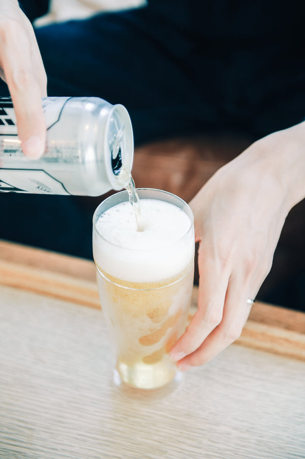 Hands tilting pitcher to pour white foam into beer glass with golden base layer