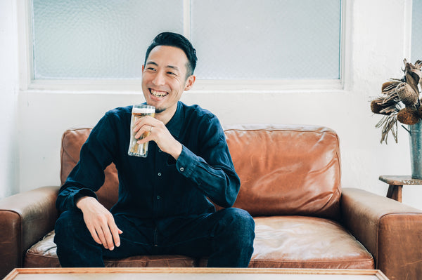 Smiling man in blue velvet shirt holding frosted beer glass on contemporary sofa