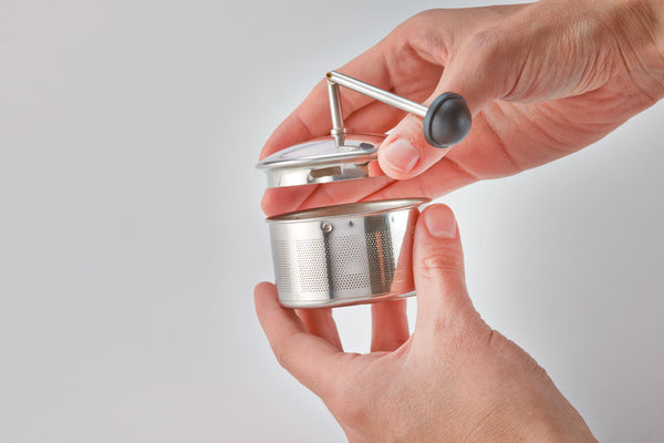 Hand holding stainless steel mesh tea infuser basket with metal pull-up mechanism
