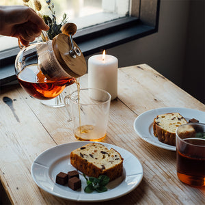 Tea service with amber glass teapot pouring into clear mug, sliced fruit cake on white plate with mint garnish