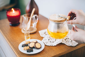 Close view of hands removing olive wood lid from glass teapot with amber tea inside