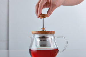 Hand pulling up wooden-handled stainless steel infuser basket from glass pot