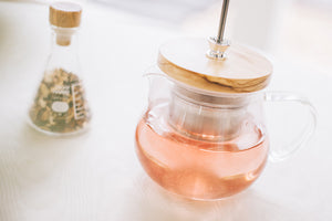 Glass teapot with wooden lid containing steeped tea, infuser handle visible