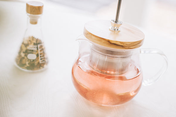 Glass teapot with wooden lid containing steeped tea, infuser handle visible
