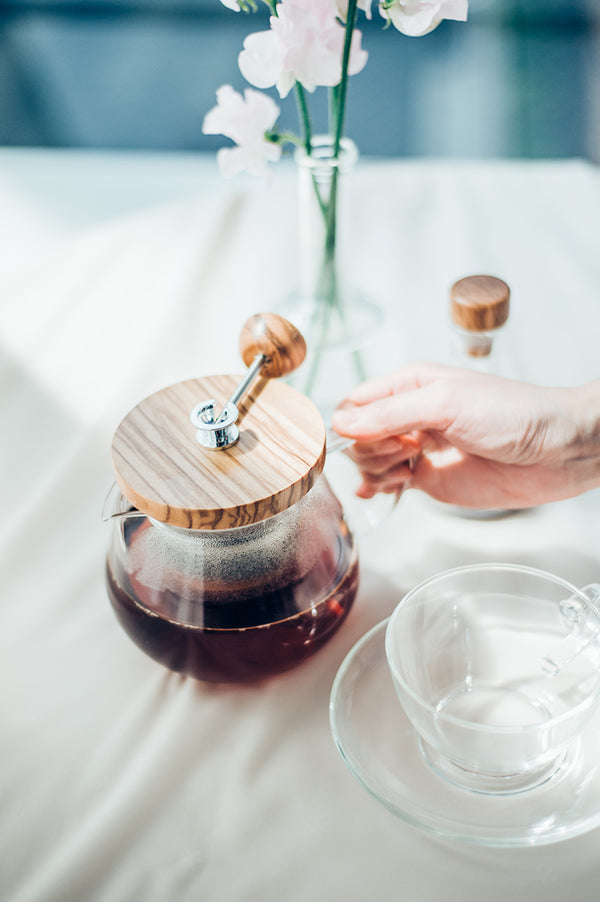 Overhead tea service with dark tea in pot with wood lid, white flowers, and ice-filled cup