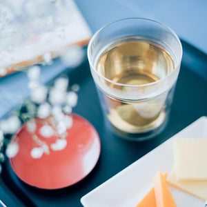 Glass of pale liquid with ice cubes on blue background with decor.