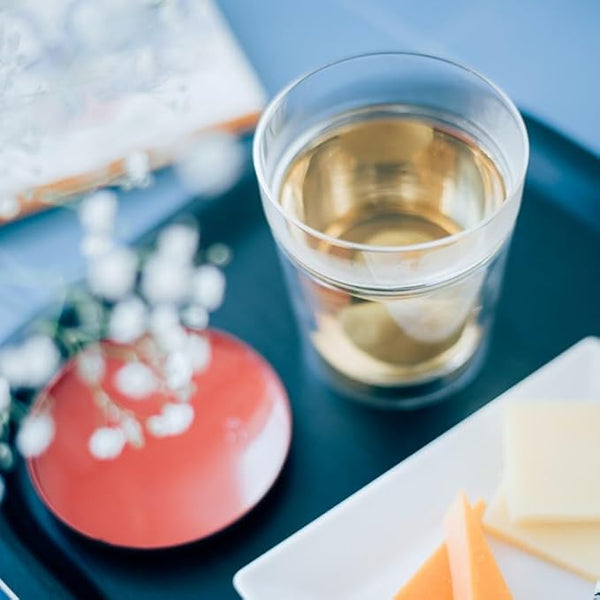Glass of pale liquid with ice cubes on blue background with decor.