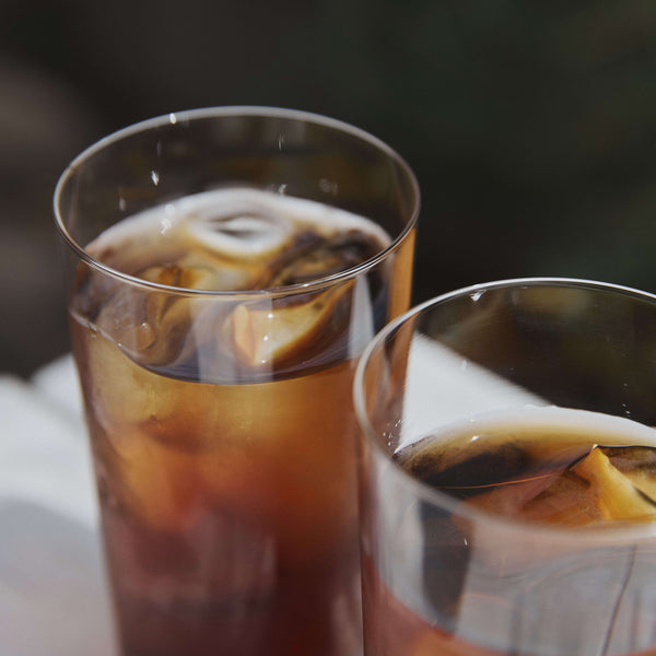 Two glasses of golden cola with ice cubes on white surface.