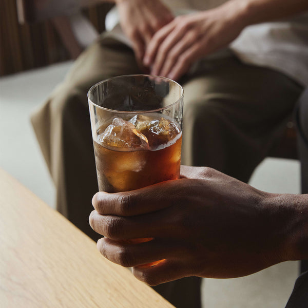 Person's hand holding glass of cola with ice on white table.
