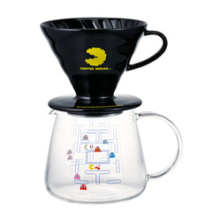 Black ceramic V60 dripper with yellow PAC-MAN graphic and glass carafe showing pixel-art maze game design below.