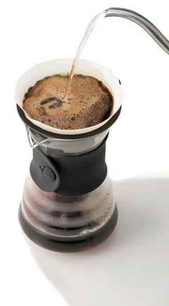 Hot water pouring into white dripper cone filled with ground coffee over glass carafe.