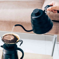 Person pouring hot water from black gooseneck kettle into coffee dripper with ground coffee.