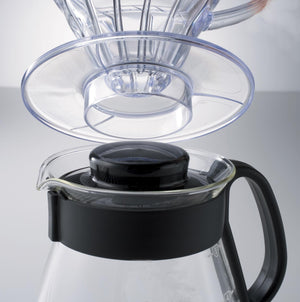 Clear glass dripper cone and reusable filter components separated above black and clear carafe base