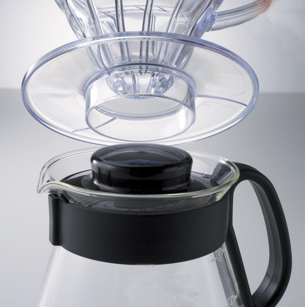 Clear glass dripper cone and reusable filter components separated above black and clear carafe base