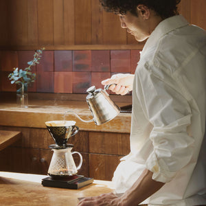 Person pouring water into V60 dripper positioned above glass carafe