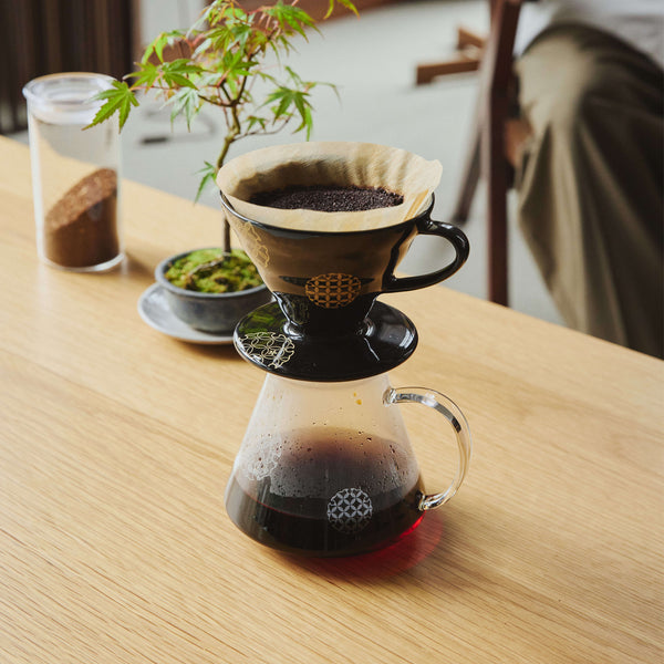 V60 dripper actively brewing coffee over glass carafe on wooden table
