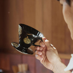 Hand holding black ceramic V60 dripper with gold Shippou pattern details