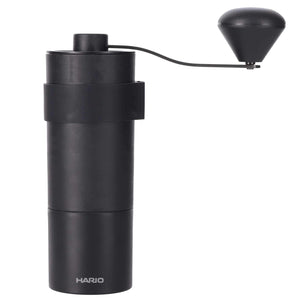 Black cylindrical Zebrang coffee grinder with attached hand crank and conical burr system, white background