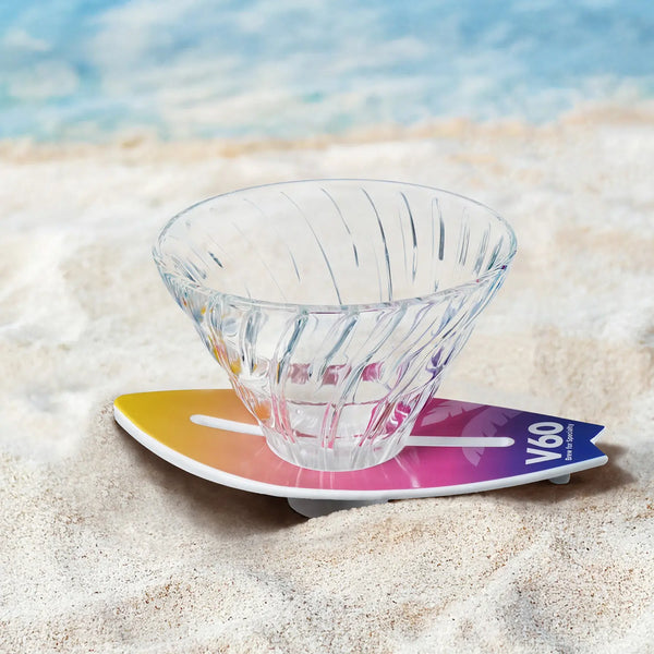 HARIO V60 Surfboard Base dripper with gradient yellow-to-purple surfboard stand on sandy beach.