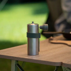 Stainless steel Hario V60 portable coffee mill with black silicone band on wooden outdoor table